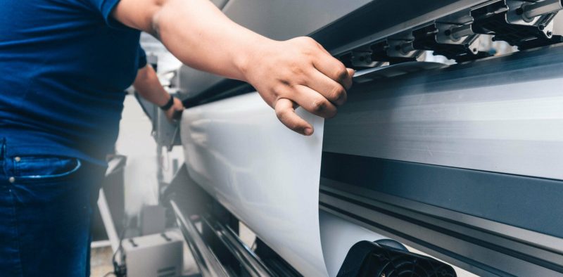 man holding printable material on alarge format printing plotter.graphic design and advertising concept.